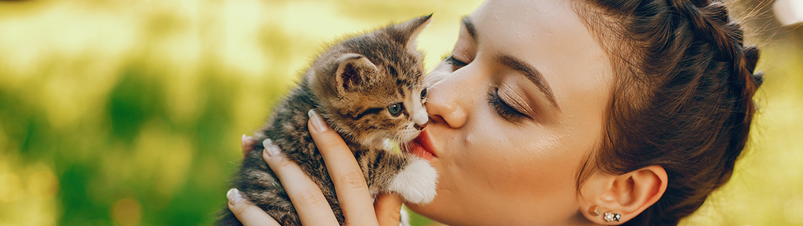 Eine Frau hebt ein kleines Kätzchen hoch und küsst es vorsichtig.