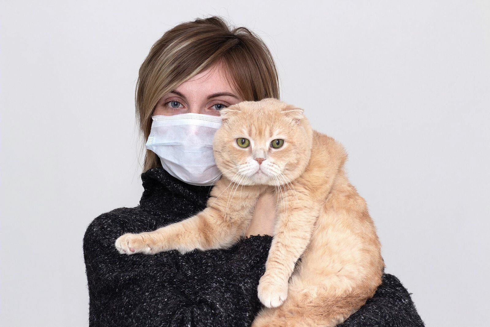 Eine Frau trägt einen Mundschutz und hält eine Katze auf dem Arm.