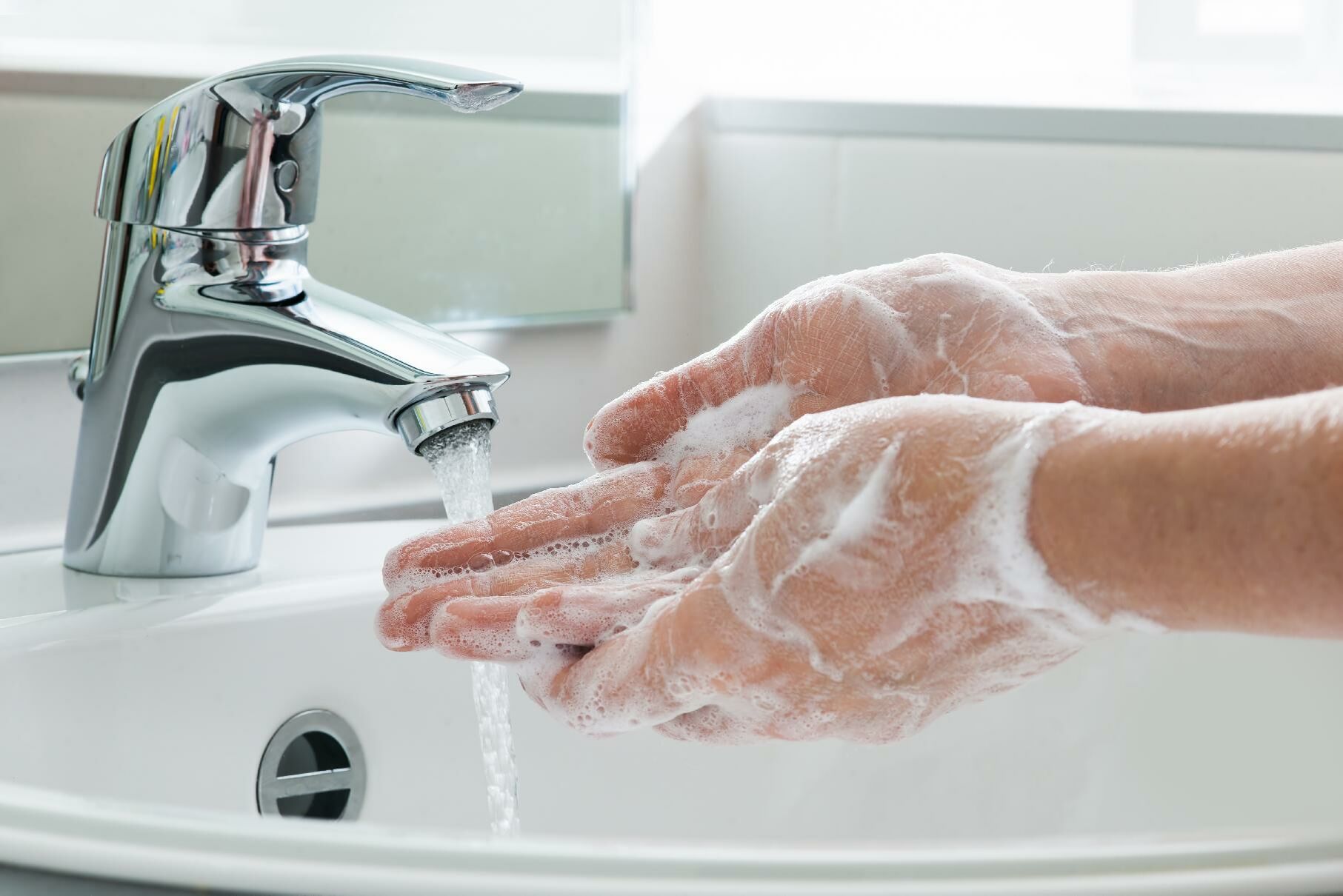 Das Wasser aus einem laufenden Wasserhahn spült Seife von zwei Händen.